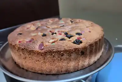 A round golden cake dotted with dried fruit on a metal stand