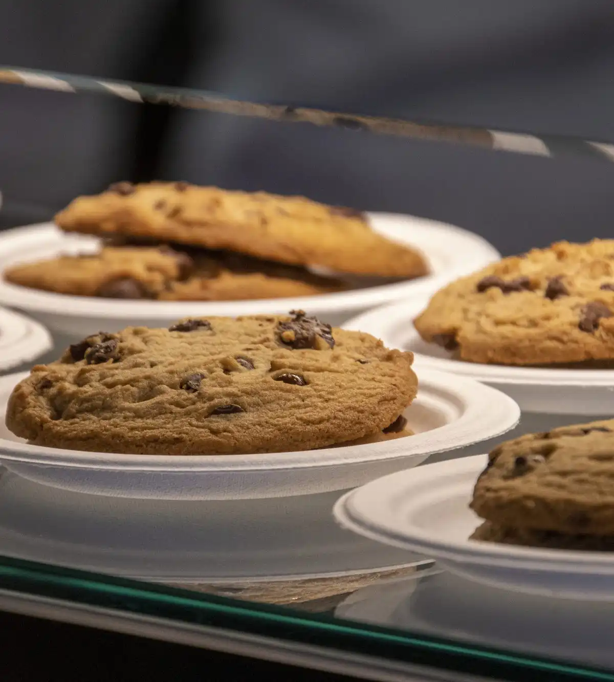 Chocolate chip cookies on small plates in a glass counter
