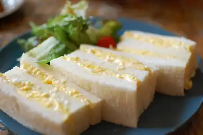 Thick-cut egg salad sandwiches on a dark plate with salad leaves