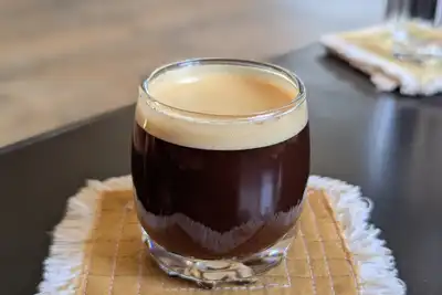 A double espresso in a small glass on a fringed coaster