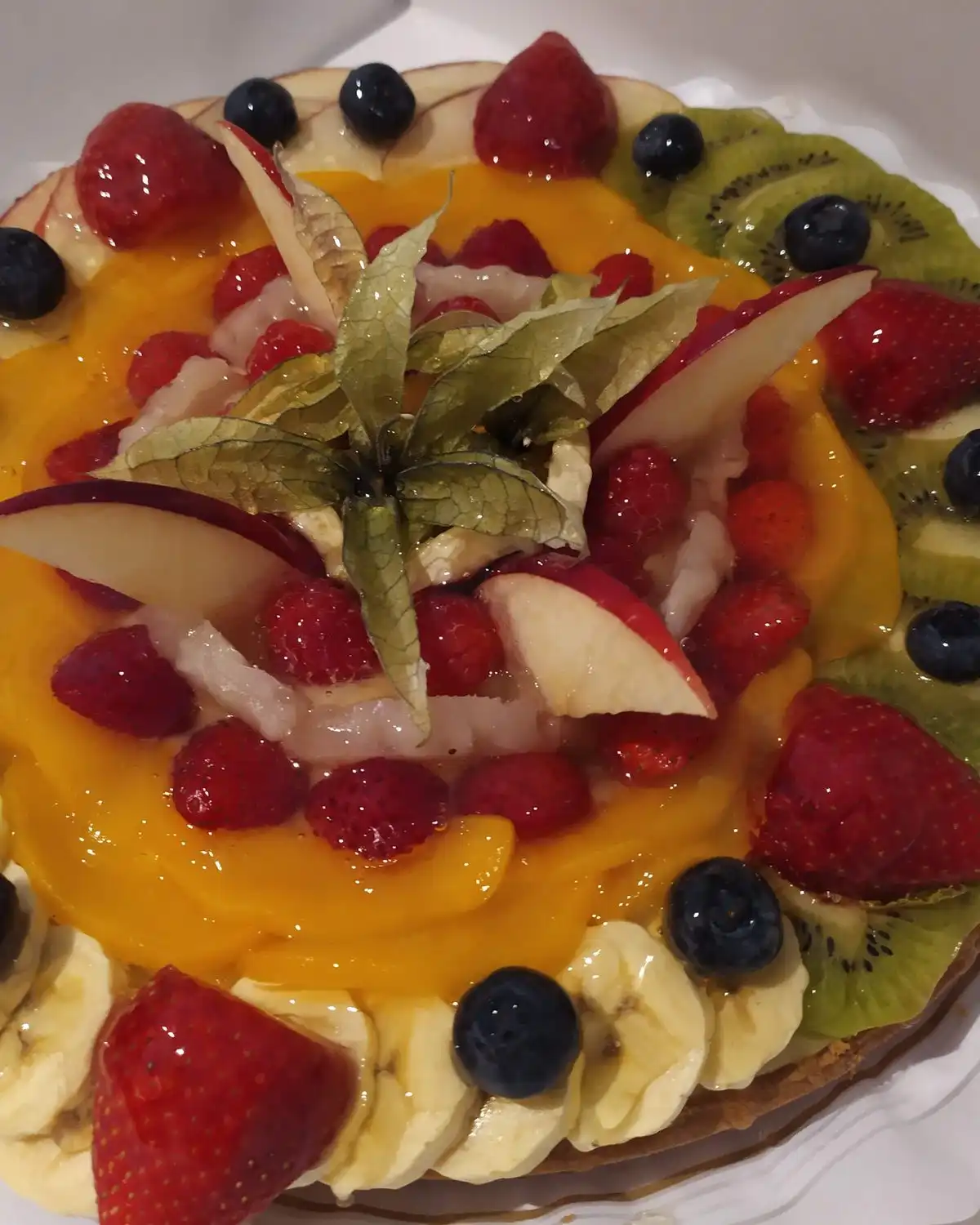 A round tart topped with strawberries, blueberries, kiwi, peach and banana