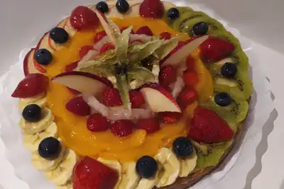 A round tart topped with strawberries, blueberries, kiwi, peach and banana