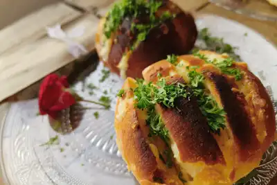 Two scored loaves with herbs and melted butter on a glass plate
