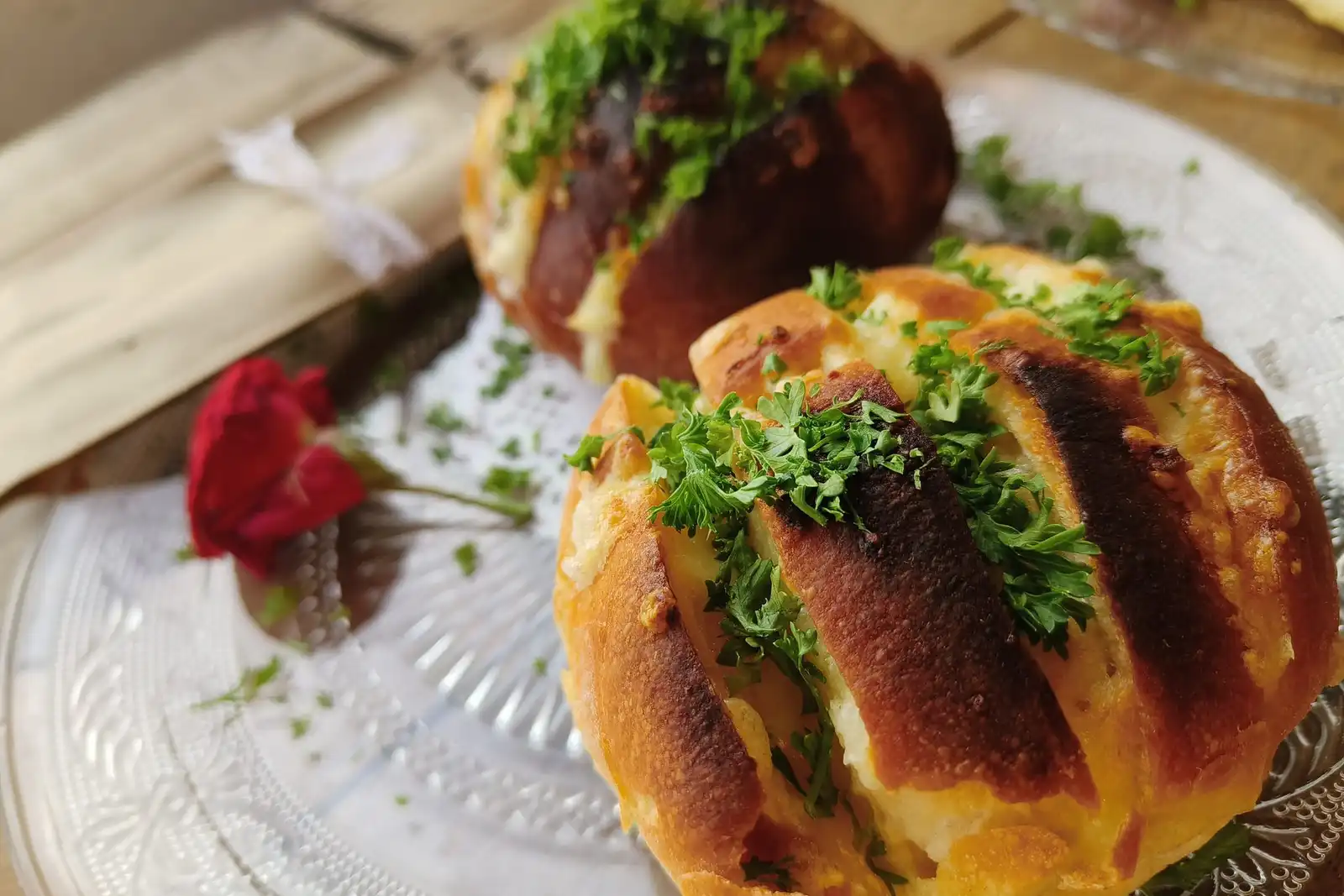 Two scored loaves with herbs and melted butter on a glass plate