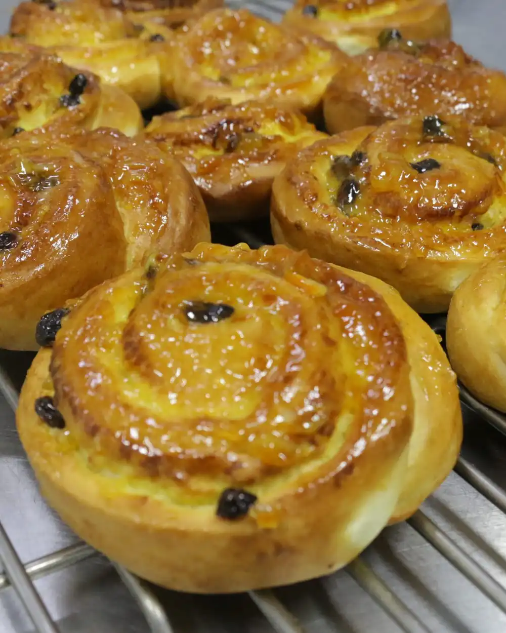 Glazed raisin swirl buns cooling on a wire rack