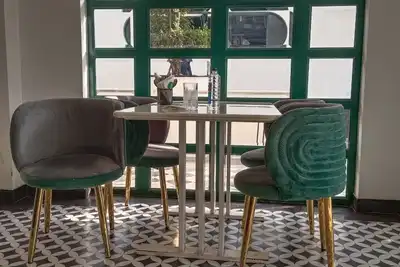 A café table with green velvet chairs in front of an arched window, on a patterned tile floor