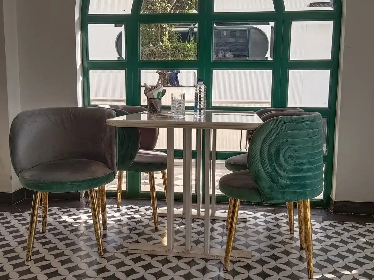 A café table with green velvet chairs in front of an arched window, on a patterned tile floor